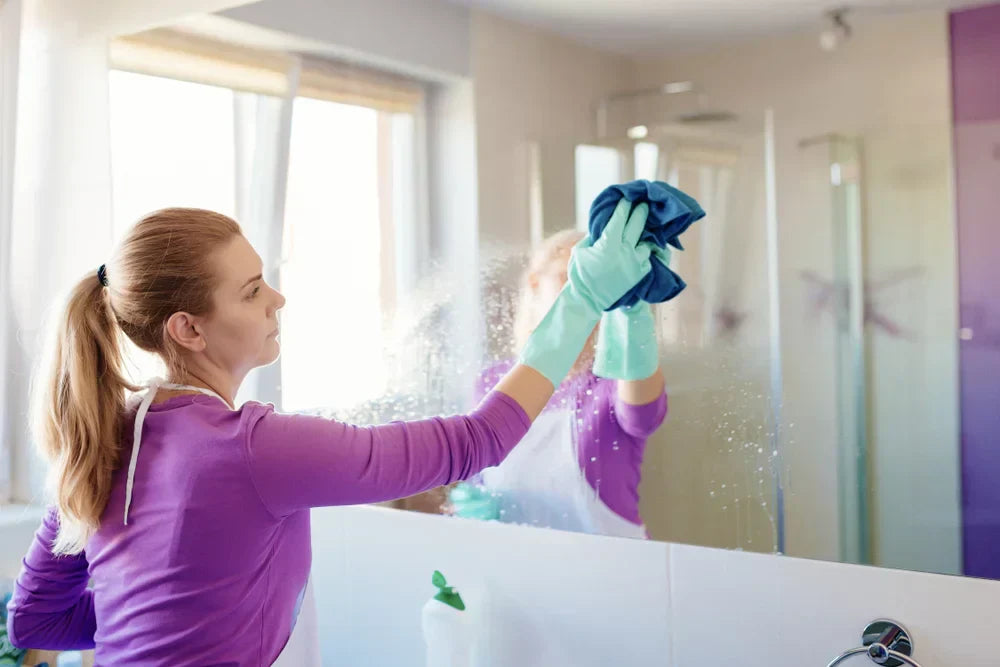 Young woman cleaning mirror in bathroom.